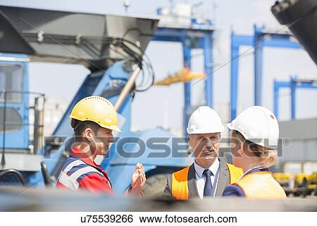 Stock Photograph - Workers discussing in shipping yard. Fotosearch
