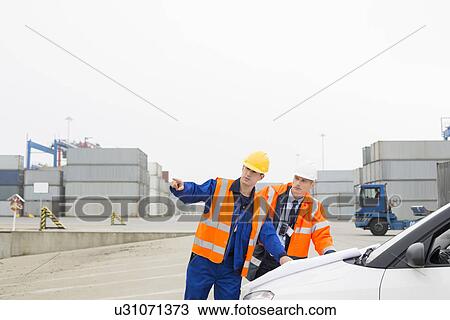 Stock Image - Workers discussing over blueprint in shipping yard. Fotosearch