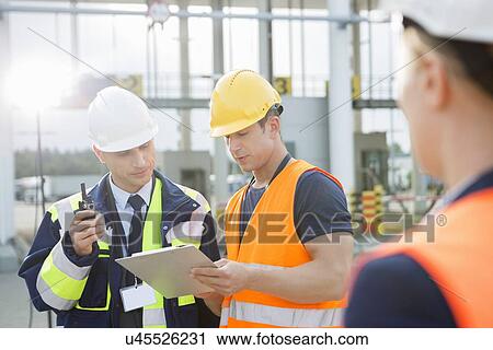 Workers discussing over clipboard in shipping yard View Large Photo Image Stock Image - Workers discussing over clipboard in shipping yard. Fotosearch
