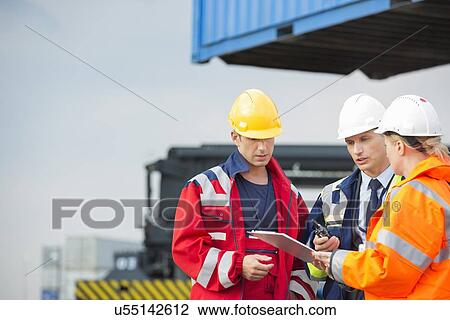 Workers discussing over clipboard in shipping yard View Large Photo Image Stock Image - Workers discussing over clipboard in shipping yard. Fotosearch