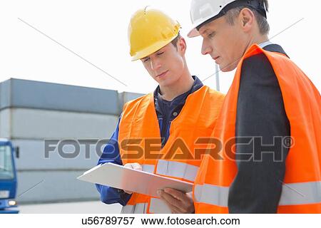 Workers discussing over clipboard in shipping yard View Large Photo Image Stock Photo - Workers discussing over clipboard in shipping yard. Fotosearch