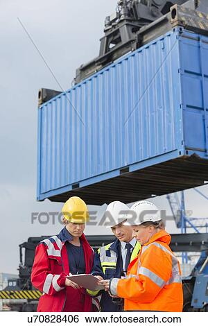 Stock Photograph - Workers discussing over clipboard in shipping yard. Fotosearch