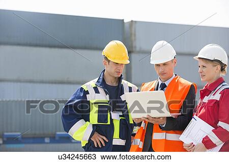 Workers discussing over laptop in shipping yard View Large Photo Image Stock Image - Workers discussing over laptop in shipping yard. Fotosearch