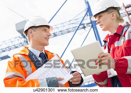 Stock Image - Workers discussing over tablet computer in shipping yard. Fotosearch