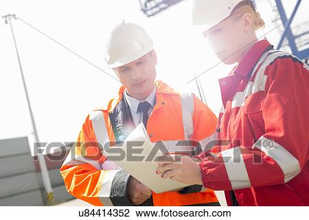 Stock Image - Workers discussing over tablet computer in shipping yard. Fotosearch