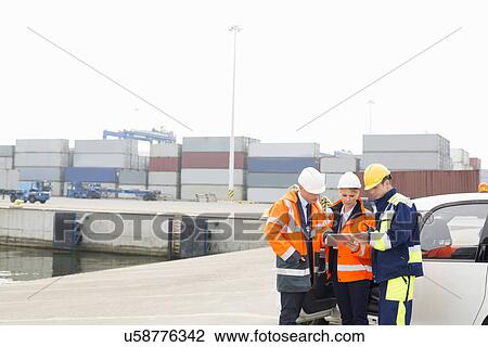 Stock Image - Workers using tablet PC beside car in shipping yard. Fotosearch