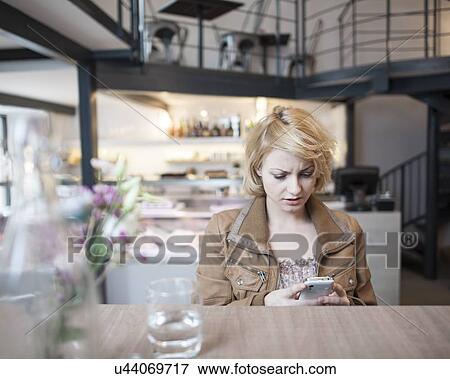 Worried young woman reading text message on cell phone in cafe View Large Photo Image Stock Photo - Worried young woman reading text message on cell phone in cafe. Fotosearch