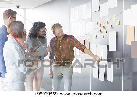 Stock Photo - Young businessman explaining document to colleagues in creative office. Fotosearch