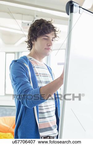 Young businessman writing on presentation board in office View Large Photo Image Stock Photo - Young businessman writing on presentation board in office. Fotosearch
