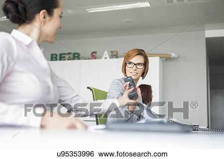 Young businesswoman handing telephone to colleague in office View Large Photo Image Stock Photograph - Young businesswoman handing telephone to colleague in office. Fotosearch