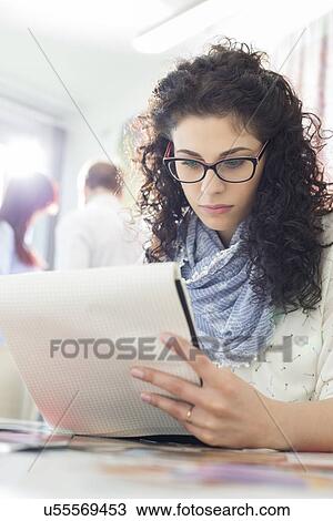 Young businesswoman reading notepad at creative office with colleagues in background View Large Photo Image Stock Image - Young businesswoman reading notepad at creative office with colleagues in background. Fotosearch