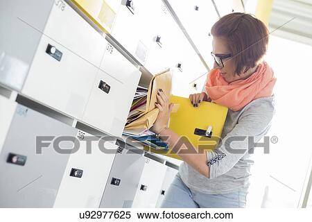 Stock Photography - Young businesswoman removing file from locker at creative office. Fotosearch