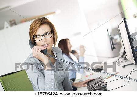 Picture - Young businesswoman talking on telephone at desk in office. Fotosearch