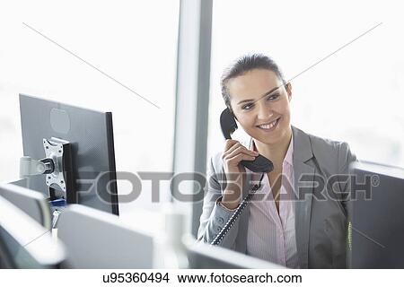 Picture - Young businesswoman talking on telephone in office. Fotosearch