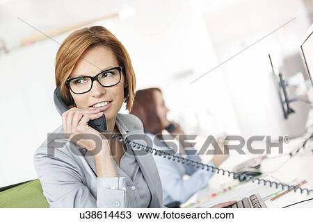 Young businesswoman talking on telephone at desk in office View Large Photo Image Stock Image - Young businesswoman talking on telephone at desk in office. Fotosearch