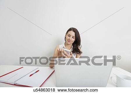 Young businesswoman using cell phone at desk in office View Large Photo Image Stock Photo - Young businesswoman using cell phone at desk in office. Fotosearch