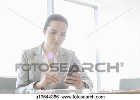 Stock Photograph - Young businesswoman using cell phone in office. Fotosearch