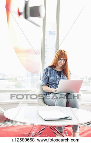 Stock Photo - Young businesswoman using laptop in creative office. Fotosearch