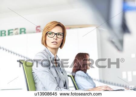 Young businesswoman working on computer with colleague in background at office View Large Photo Image Stock Photography - Young businesswoman working on computer with colleague in background at office. Fotosearch