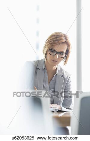 Young businesswoman writing at desk in office View Large Photo Image Stock Photography - Young businesswoman writing at desk in office. Fotosearch