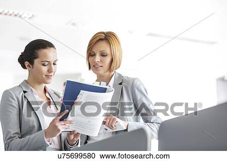 Young businesswomen discussing over book in office View Large Photo Image Stock Image - Young businesswomen discussing over book in office. Fotosearch