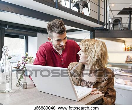 Young couple looking at each other while using laptop in cafe View Large Photo Image Stock Photo - Young couple looking at each other while using laptop in cafe. Fotosearch