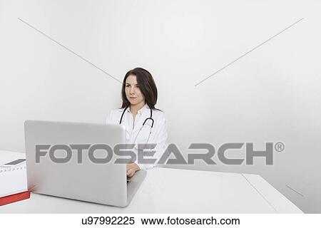 Young female doctor looking away while using laptop at desk in clinic View Large Photo Image Stock Photography - Young female doctor looking away while using laptop at desk in clinic. Fotosearch