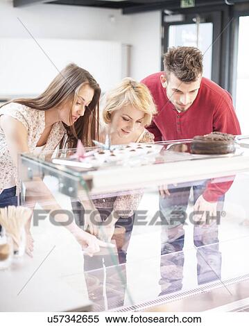 Stock Photography - Young friends looking at display cabinet at cafe. Fotosearch