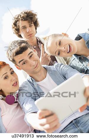 Young friends photographing themselves through digital tablet at university campus View Large Photo Image Stock Image - Young friends photographing themselves through digital tablet at university campus. Fotosearch