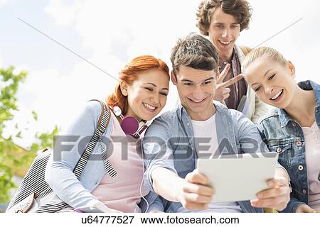 Young friends photographing themselves through digital tablet at college campus View Large Photo Image Stock Photo - Young friends photographing themselves through digital tablet at college campus. Fotosearch