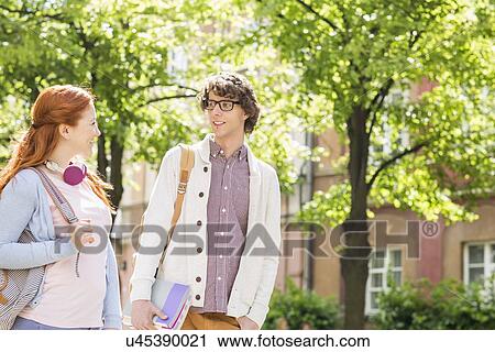 Stock Image - Young male and female college students talking while walking on street. Fotosearch