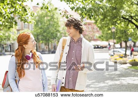 Stock Image - Young male and female college students talking while walking on footpath. Fotosearch