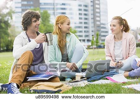 Stock Photo - Young man having coffee while studying with female friends at college campus. Fotosearch