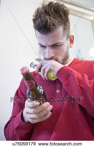 Stock Photo - Young man reading label on beer bottle in cafe. Fotosearch