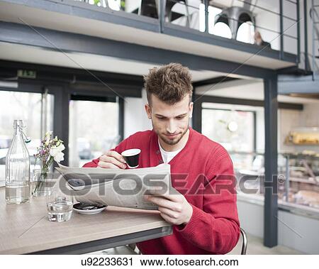 Young man reading newspaper while drinking coffee in cafe View Large Photo Image Stock Image - Young man reading newspaper while drinking coffee in cafe. Fotosearch