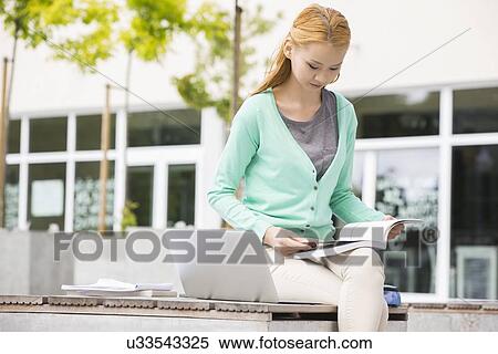 Stock Photography - Young woman reading book at college campus. Fotosearch