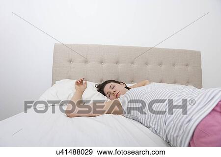 Stock Photo - Young woman sleeping comfortably in bed. Fotosearch