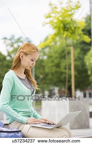 Stock Photo - Young woman using laptop at college campus. Fotosearch
