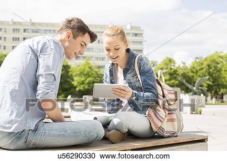 Stock Image - Young woman with male friend using digital tablet at college campus. Fotosearch