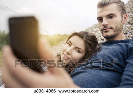 Stock Photograph - Attractive young couple posing for selfie on smartphone. Fotosearch