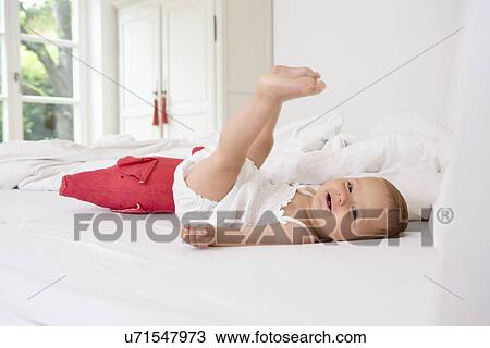 Stock Image - Baby girl lying on bed with legs raised. Fotosearch