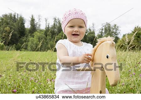 Picture - Baby girl playing on hobby horse. Fotosearch