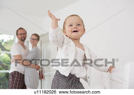 Baby with hand raised, parents in background View Large Photo Image Stock Photograph - Baby with hand raised, parents in background. Fotosearch
