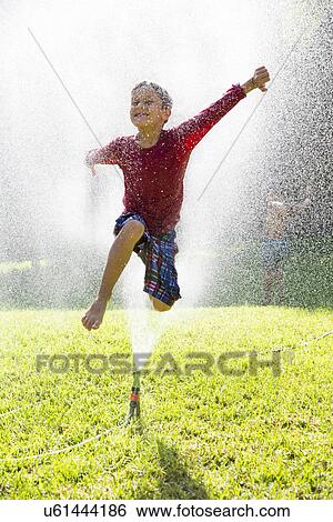 Boy jumping over water sprinkler in garden View Large Photo Image Stock Photograph - Boy jumping over water sprinkler in garden. Fotosearch