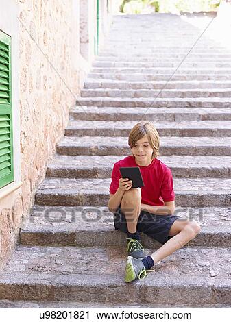 Boy looking at digital tablet on village steps, Majorca, Spain View Large Photo Image Stock Image - Boy looking at digital tablet on village steps, Majorca, Spain. Fotosearch