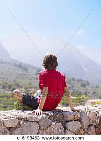 Boy sitting on stone wall gazing at view, Majorca, Spain View Large Photo Image Stock Image - Boy sitting on stone wall gazing at view, Majorca, Spain. Fotosearch
