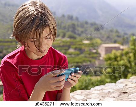 Stock Image - Boy sitting on stone wall looking at smartphone, Majorca, Spain. Fotosearch