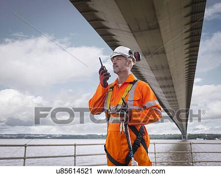 Stock Image - Bridge worker using walkie-talkie under suspension bridge. The Humber Bridge, UK was built in 1981 and at the time was the world's largest single-span suspension bridge. Fotosearch