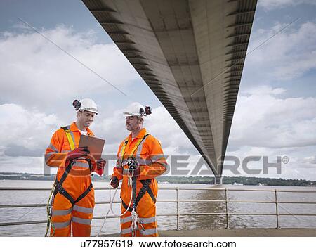 Stock Photo - Bridge workers in meeting under suspension bridge. The Humber Bridge, UK was built in 1981 and at the time was the world's largest single-span suspension bridge. Fotosearch