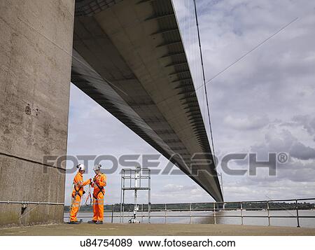 Stock Photo - Bridge workers meeting under suspension bridge. The Humber Bridge, UK was built in 1981 and at the time was the world's largest single-span suspension bridge. Fotosearch